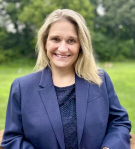 Laura Olson, new CEO, poses outdoors in a navy blue blazer. Olson brings a leadership style rooted in listening and deep community connections.