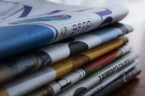 Stack of folded newspapers on a wooden surface, shown in close-up with selective focus